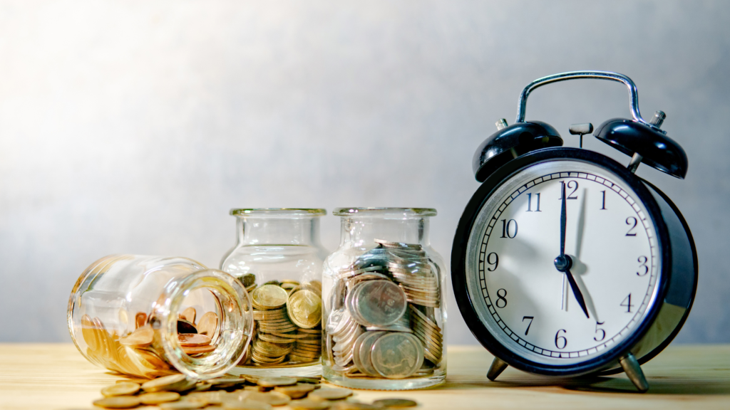 “Stacked coins in glass jars beside an alarm clock symbolizing time, savings, and financial planning.”