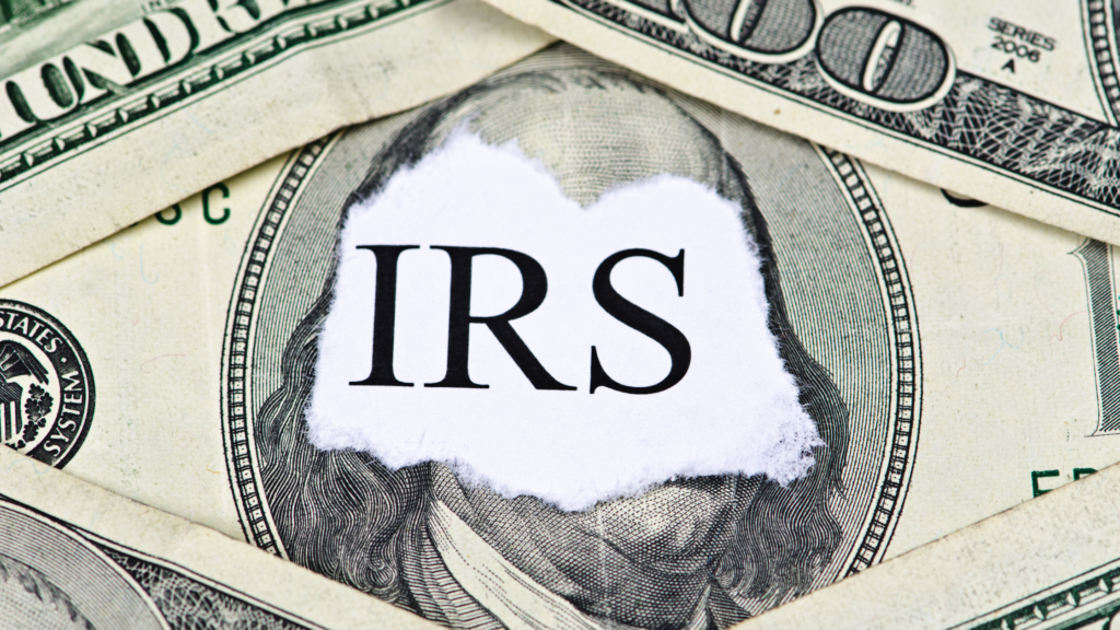 The word “IRS” on torn paper placed over U.S. dollar bills.